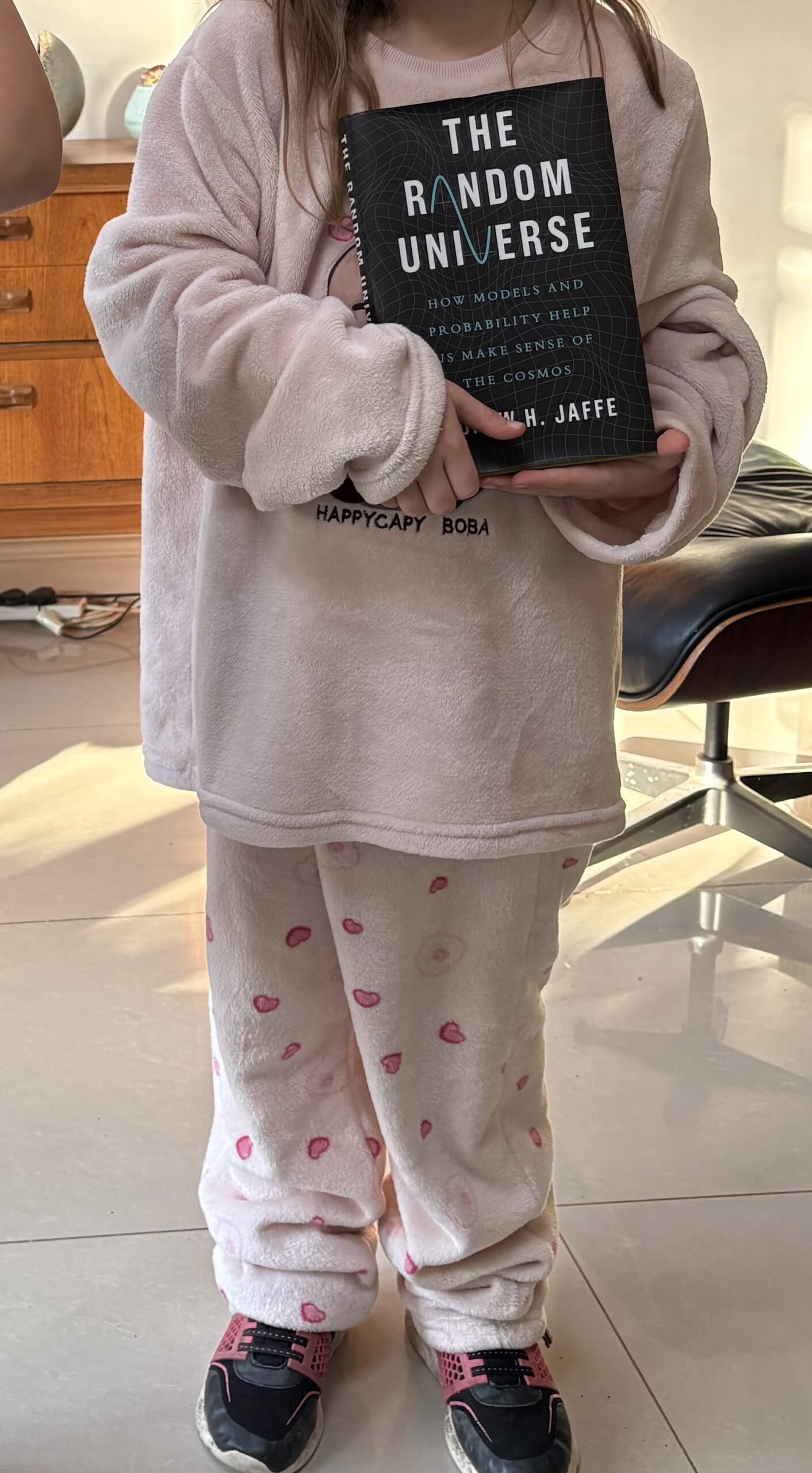 Child in pink pyjamas holding a copy of The Random Universe by Andrew H. Jaffe