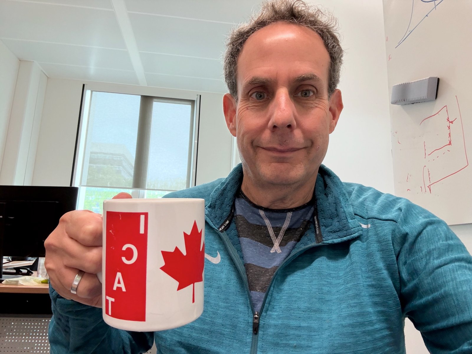 Man in blue shirt holding a white mug with a red maple leaf and the letters “ICAT” in white on red.